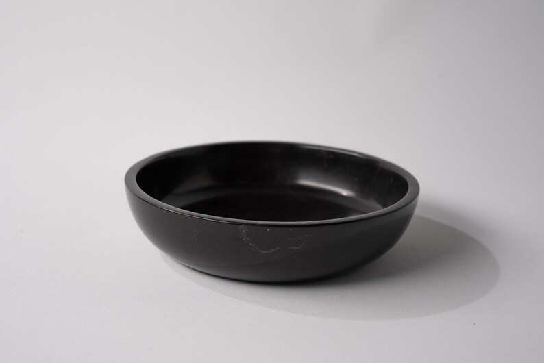 May include: A black, round, shallow bowl made of marble. The bowl has a smooth, polished surface.