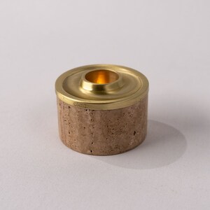 May include: A small, round, beige candle holder with a brass top. The top has a small, round opening for a candle.