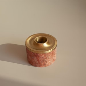 以下が含まれることがあります： 金色の金属製の蓋が付いた、小さく丸い赤い大理石のキャンドルホルダー。蓋の中央にはキャンドル用の小さな穴があります。