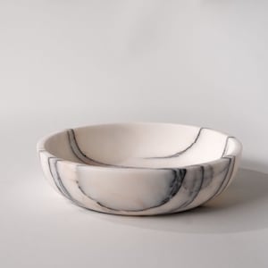 May include: A white marble bowl with black veining. The bowl is round and has a smooth, polished surface.