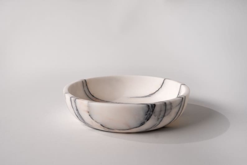 May include: A white marble bowl with black veining. The bowl is round and has a smooth, polished surface.