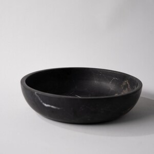 May include: A black marble bowl with white veining. The bowl is round and has a smooth, polished finish.