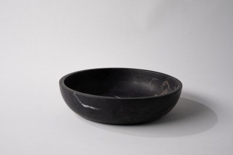 May include: A black marble bowl with white veining. The bowl is round and has a smooth, polished finish.