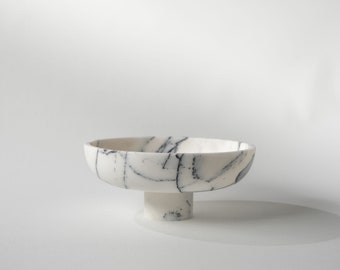 May include: A white ceramic bowl with black marbling. The bowl has a wide, shallow base and a tall, cylindrical pedestal.