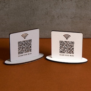 May include: Two white wooden signs with a black border and a black Wi-Fi symbol. Each sign has a black and white QR code and the text "SCAN FOR WIFI".
