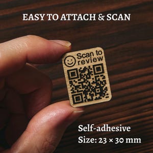 Op de afbeelding: Een kleine, zelfklevende houten tag met een QR-code en de tekst "Scan to review". De tag is rechthoekig, met afgeronde hoeken en meet 2,3 x 3,0 cm. De tekst "Easy to attach & scan" staat bovenaan.