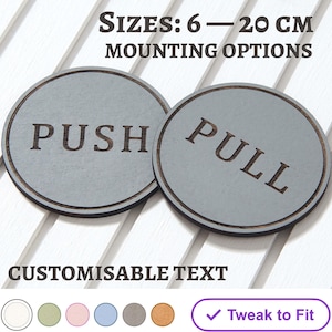 May include: Two gray circular door signs with the words "PUSH" and "PULL" in a dark font. The signs are 6-20 cm in size and have customizable text. The signs are on a white slatted surface.