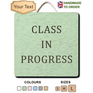 Op de afbeelding: Een vierkant lichtgroen houten bord met een wit touw om op te hangen. De tekst CLASS IN PROGRESS staat in donkerbruine hoofdletters op het bord. Erboven bevindt zich een beige label met de tekst Your Text en een Britse vlag met HANDMADE TO ORDER.