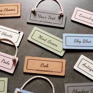 Puede incluir: Un conjunto de etiquetas de madera de varios colores y con texto. Las etiquetas sirven para etiquetar artículos como cápsulas de lavado, sábanas, aperitivos y clases de pintura. Las etiquetas están hechas de madera natural y tienen un aspecto rústico.