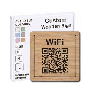 May include: A square light brown wooden sign featuring the black text WiFi and a black QR code. Behind the sign is a white product box labelled Custom Wooden Sign with sections for Available Colours, Sizes S, M, L, and Mounting Options.