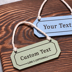 May include: Two wooden gift tags with twine hanging loops. The top tag is light blue with the text "Your Text". The bottom tag is green with the text "Custom Text" and "LINE 2 (OPTIONAL)".