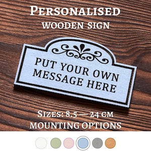 May include: A rectangular wooden sign with an arched top and decorative scrollwork. The sign features the black text "PUT YOUR OWN MESSAGE HERE" and indicates available sizes from 8.5 to 24 cm. Below the sign, six circular color swatches are displayed.