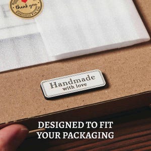 May include: A brown cardboard box with white packing material and a small rectangular sticker that reads "Handmade with love." A round sticker with the words "thank you" is also visible.