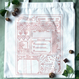 May include: White canvas tote bag featuring a detailed character sheet design in red. The sheet includes sections for stats, abilities, spells, and inventory, with decorative hearts and text like "Character Name" and "Abilities". Dice and greenery surround the bag.