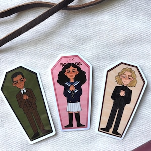 May include: Three coffin-shaped stickers featuring cartoon characters. One in a brown suit, one in a school uniform, and one in a black suit. The stickers have white borders and are set against a white background.