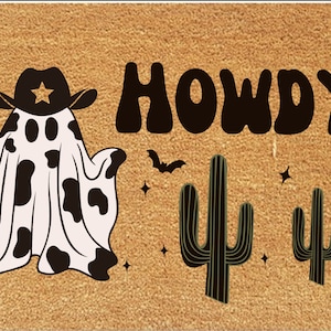 Pu&ograve; includere: Un zerbino rettangolare con sfondo beige presenta un fantasma con cappello da cowboy con una stella e un motivo a mucca. La parola "HOWDY" &egrave; in grandi lettere marrone scuro, con pipistrelli, cactus e stelle.