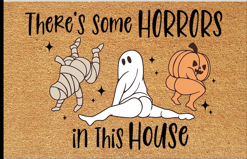 Pu&ograve; includere: Zerbino rettangolare con sfondo beige e testo nero che recita "There's some HORRORS in This HOUSE." Il tappetino presenta illustrazioni di cartoni animati di una mummia, un fantasma e una zucca.