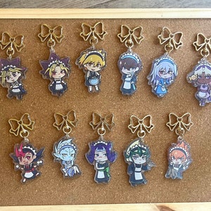 Peut inclure: Dix breloques de personnages d'anime colorés avec des nœuds et des chaînes dorés. Chaque breloque représente un personnage différent en tenue de femme de chambre. Les personnages sont tous dans un style chibi.