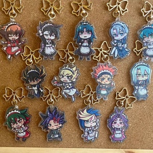 Könnte beinhalten: Eine Sammlung von 12 bunten Anime-Charakter-Anhängern mit Figuren in Dienstmädchen-Outfits. Die Anhänger sind an goldenen Schleifen befestigt und werden auf einer Korktafel ausgestellt.