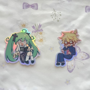 May include: Two iridescent stickers featuring anime characters. The first sticker shows a girl with green hair and a book that says "YADRI NOTE". The second sticker shows a boy with blonde hair and a book.