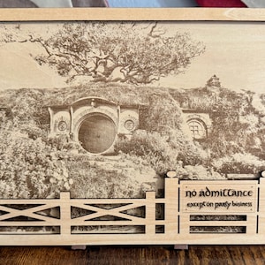 May include: A wooden sign with a laser-engraved image of a hobbit house with a round door and a sign that reads "No admittance except on party business".
