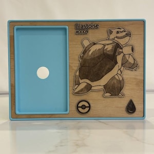 May include: A wooden frame with a blue interior and a detailed engraving of a Blastoise character. The text "Blastoise #0009" is visible. The frame also features a Pokemon symbol and a water drop icon.