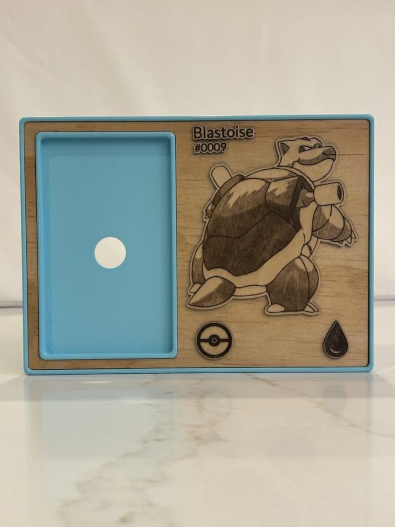 May include: A wooden frame with a blue interior and a detailed engraving of a Blastoise character. The text "Blastoise #0009" is visible. The frame also features a Pokemon symbol and a water drop icon.