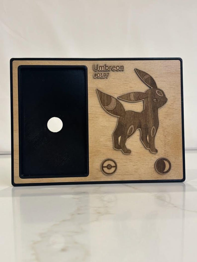 May include: Wooden Umbreon Pok&eacute;mon card holder with a black interior and a light wood exterior. The design features the Umbreon character, the name "Umbreon" and the number "#0197". Includes a Pok&eacute; Ball and moon symbol.