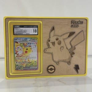 May include: A wooden display frame with a yellow border, holding a graded Pikachu Pok&eacute;mon card. The card is in a protective case, graded as Gem Mint 10. A Pikachu illustration and text "Pikachu #0025" are etched on the wood.