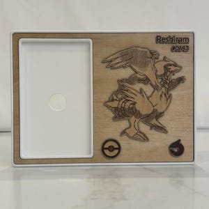May include: Wooden frame with a white interior and a laser-cut design of Reshiram, a character from the Pok&eacute;mon series. The frame includes the text "Reshiram #0643" and two circular symbols.