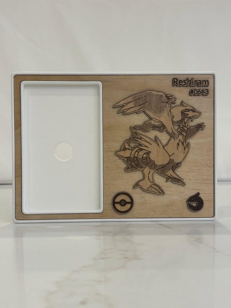 May include: Wooden frame with a white interior and a laser-cut design of Reshiram, a character from the Pok&eacute;mon series. The frame includes the text "Reshiram #0643" and two circular symbols.