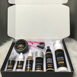Può includere: Una scatola nera con una varietà di prodotti per la cura dei capelli, tra cui controllo dei bordi, colla per pizzo, olio per la crescita dei capelli, stick di cera, spray per la tinta del pizzo e mousse per capelli. I prodotti sono tutti in un packaging nero e oro con il nome del marchio "Hair Universal" stampato su di essi.