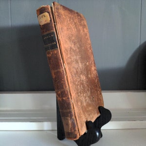 May include: A worn, brown leather-bound book with a spine label that reads "Hall, Sr. Sermons". The book is on a black book stand.
