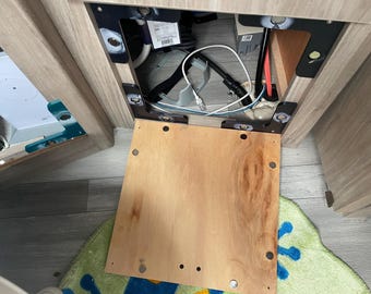 May include: A wooden access panel with multiple screws and a small opening revealing wires and electrical components.