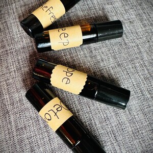 May include: Four small glass roller bottles with black caps and brown labels. The labels have handwritten text that reads "Refresh", "Sleep", "Hope", and "Joy".