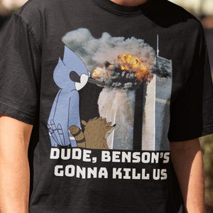Op de afbeelding: Zwart T-shirt met een cartoonafbeelding van twee personages uit de animatieserie Regular Show, en de tekst "DUDE, BENSON'S GONNA KILL US". De afbeelding toont een scène van vernietiging.