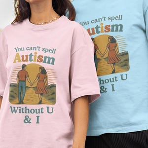 May include: Two people wearing matching t-shirts. One is pale pink, the other is light blue. Both shirts feature the text "You can't spell Autism Without U & I" with a graphic of two people holding hands.