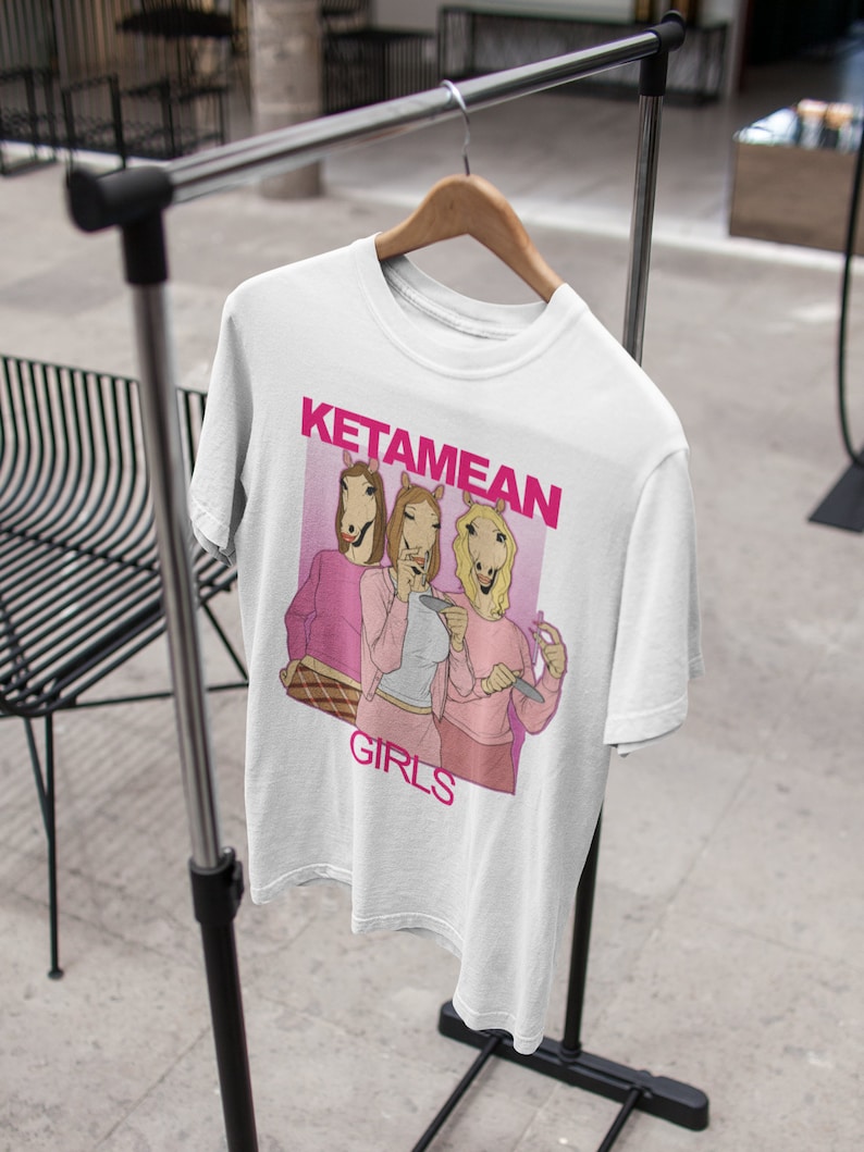 May include: White t-shirt with a pink graphic of three women with horse heads. The graphic says "KetameAn Girls".