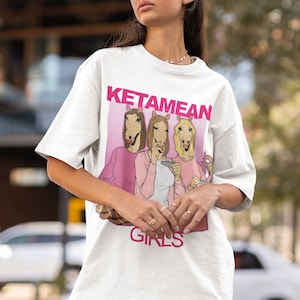 May include: White t-shirt with a pink graphic of three women with horse heads. The graphic says "Ketamean Girls".