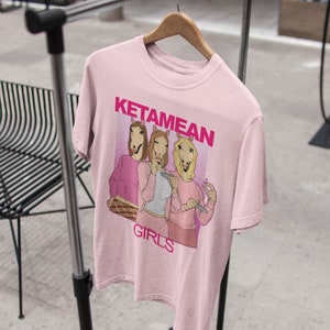 May include: Pink t-shirt with a graphic of three women with horse heads wearing pink outfits and the text "Ketamine Girls".