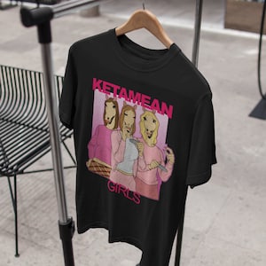 May include: Black t-shirt with a pink graphic of three women wearing horse heads. The graphic says "Ketamine Girls".