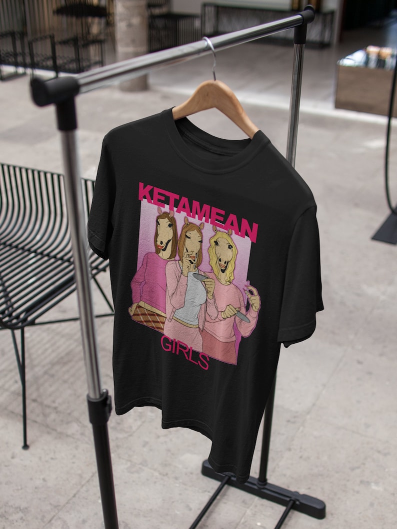 May include: Black t-shirt with a pink graphic of three women wearing horse heads. The graphic says "Ketamine Girls".