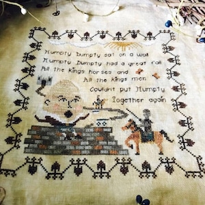 May include: Cross-stitch embroidery of the nursery rhyme "Humpty Dumpty" with a colourful illustration of Humpty Dumpty falling off a wall and a king on horseback. The text reads: "Humpty Dumpty sat on a wall, Humpty Dumpty had a great fall, All the king's horses and all the king's men, Couldn't put Humpty together again."