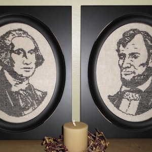 May include: Two framed portraits of historical figures, George Washington and Abraham Lincoln, in black frames with oval-shaped openings. The portraits are stitched in black thread on a beige fabric background.
