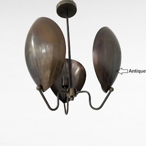 Könnte beinhalten: Ein Vintage-Kronleuchter mit antiker Patina. Die Leuchte hat drei große, oval geformte Schirme in Bronzefarbe. Die Schirme sind an einem zentralen Stiel mit gebogenen Armen aufgehängt. Das Design ist modern.