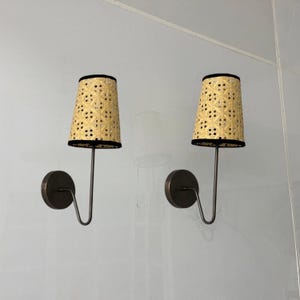 Op de afbeelding: Twee wandlampen met zwarte metalen armen en geweven rotan lampenkappen met zwarte rand.