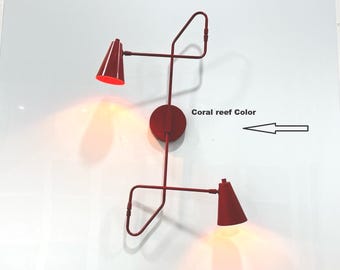 May include: A modern wall sconce in coral reef colour. The sconce features two cone-shaped lamps with a circular base and a series of curved arms. The text "Coral reef Color" is visible.