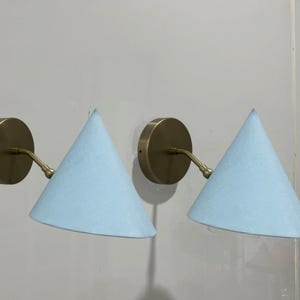 May include: A pair of brass wall lights with light blue fabric cone shades. The lights have a simple, modern design.