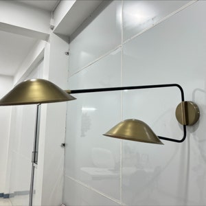 May include: A gold wall sconce with two adjustable shades. The sconce has a black metal arm and a gold base.