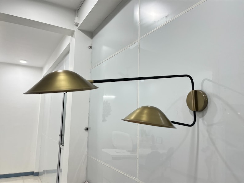 May include: A gold wall sconce with two adjustable shades. The sconce has a black metal arm and a gold base.